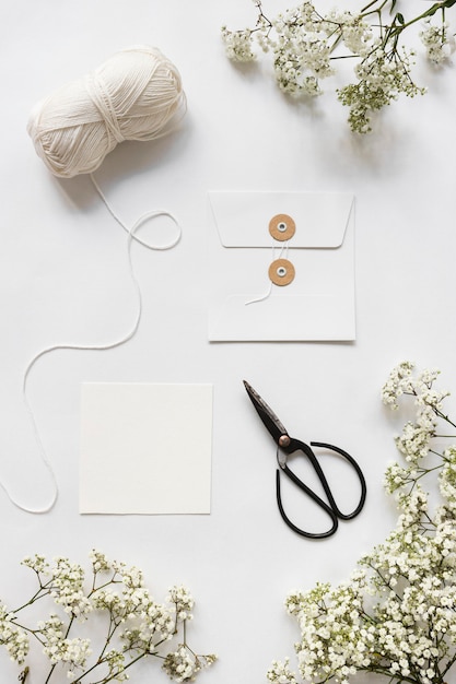 Photo gratuite pelote de laine; ciseaux; enveloppe et fleurs de souffle de bébé sur fond blanc