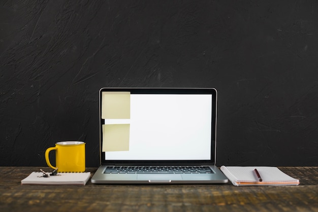 Pense-bête sur un ordinateur portable à écran blanc avec une tasse à café et des papeteries sur la table en bois