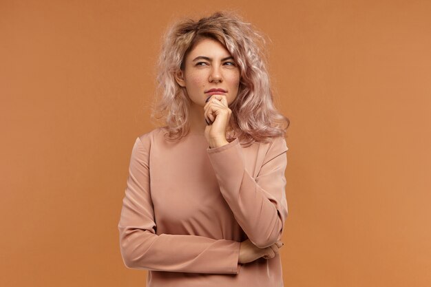 Pensées, idées et concept de considération. Portrait de fille pensive hipster avec anneau de nez et coiffure en désordre rétrécissant les yeux et toucher le menton