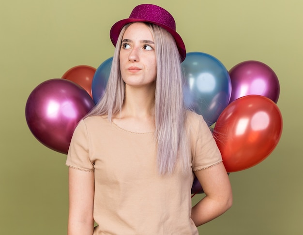 Penser la belle jeune fille portant un chapeau de fête debout derrière des ballons