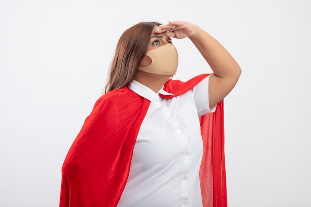 Penser les femmes de super-héros d'âge moyen portant un masque médical regardant à distance avec la main isolé sur blanc