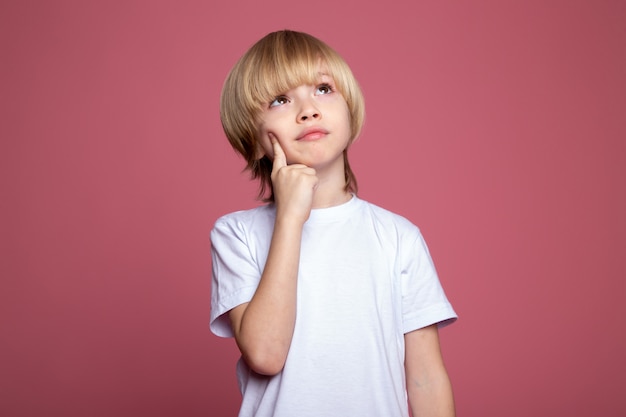 Penser garçon mignon adorable blonde en t-shirt blanc sur mur rose