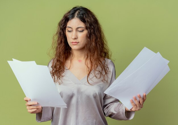 Penser jeune employé de bureau jolie femme tenant et regardant des papiers isolés sur vert olive