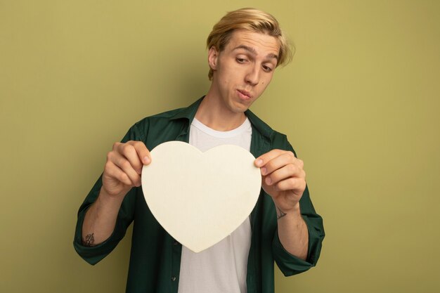 Penser jeune homme blond portant un t-shirt vert tenant et regardant la boîte en forme de coeur