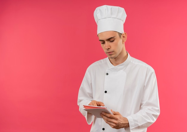 Penser jeune homme cuisinier portant l'uniforme de chef tenant et regardant le cahier avec copie espace