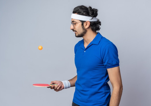 Penser un jeune homme sportif portant un bandeau avec un bracelet tenant et regardant une balle de ping-pong sur une raquette