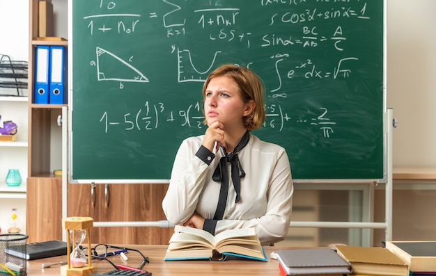 Penser qu'une jeune enseignante est assise à table avec des outils scolaires saisis le menton en classe