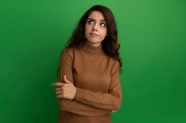 Penser en regardant côté jeune belle fille traversant les mains isolés sur un mur vert avec espace copie