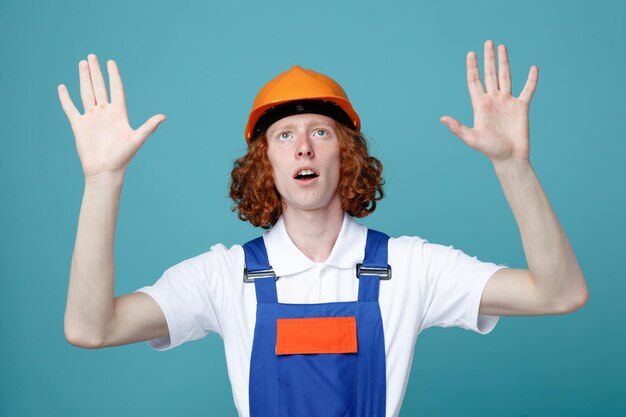 Penser répandre les mains jeune constructeur homme en uniforme isolé sur fond bleu