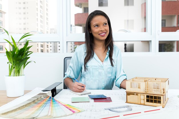 Pensif dame afro-américaine sur une chaise, prenant des notes près du plan et modèle de maison sur la table