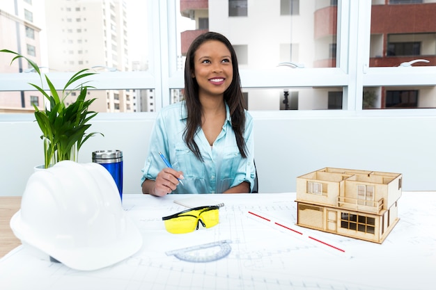 Photo gratuite pensif dame afro-américaine sur une chaise près du casque de sécurité et modèle de maison sur la table