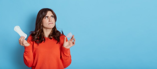 Pensive belle femme portant un pull orange décontracté à la recherche de suite avec une expression faciale réfléchie