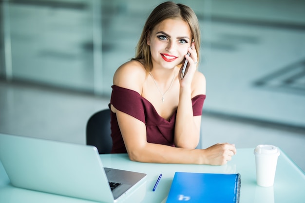 Pensive jeune femme appelant à l'opérateur du logiciel de mise à jour du support client sur ordinateur portable au bureau. Indépendante sérieuse concentrée sur une conversation téléphonique sur les affaires en ligne