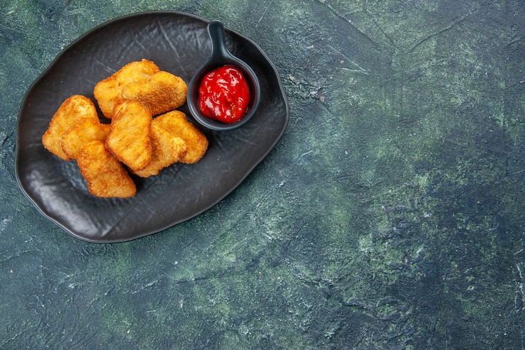 Photo gratuit pépites de poulet savoureuses et ketchup dans des assiettes noires sur le côté droit sur une surface sombre
