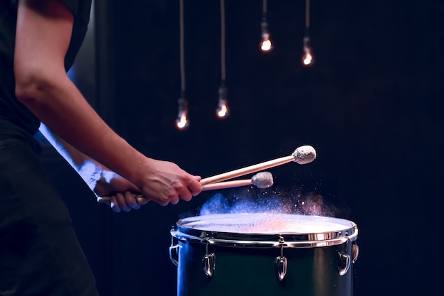 Photo gratuite le percussionniste joue avec des bâtons sur le tom au sol dans une pièce sombre avec un bel éclairage. concept de concert et de performance.