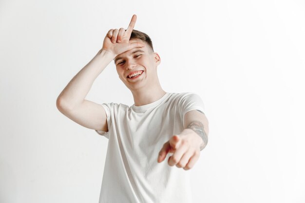 Les perdants rentrent chez eux. Portrait of happy guy montrant le signe du perdant sur le front et souriant à cause de la victoire et de rire sur fond gris