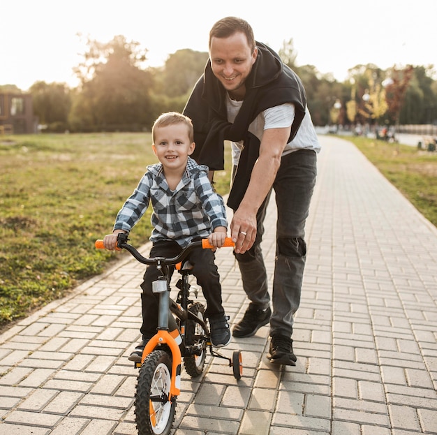 Photo gratuite père aidant son fils à faire du vélo