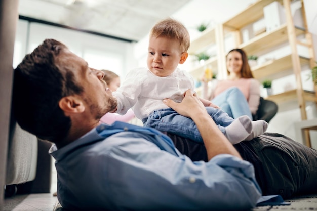 Photo gratuite père attentionné allongé sur le sol et tenant son petit garçon mère et fille sont en arrière-plan