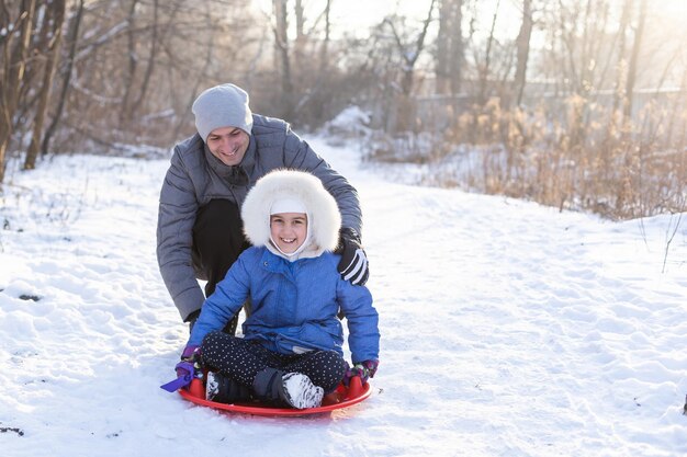 Père et enfants à cheval sur un traîneau à glace, la famille s'amuse dans la nature hivernale