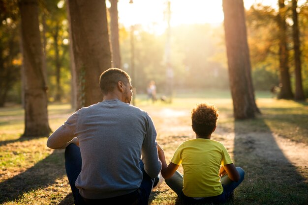 Père et fille assis sur l'herbe dans le parc profitant du coucher du soleil ensemble