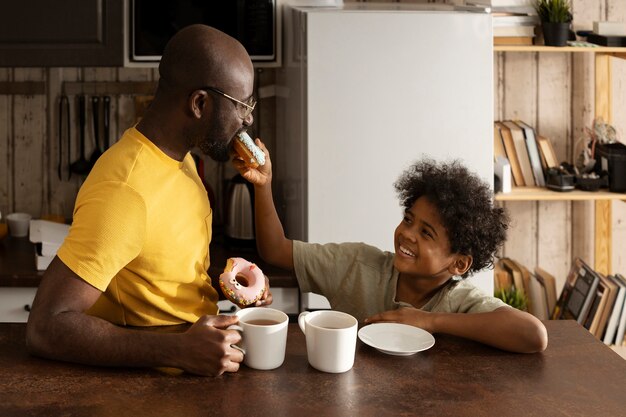 Père et fils dégustant des beignets et du thé ensemble à la maison