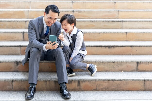 Père et fils jouant au téléphone intelligent ensemble sur le quartier des affaires urbain