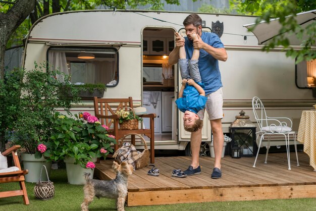 Père de loin jouant avec son fils à côté d'une caravane