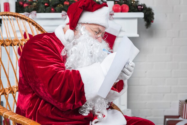 Père Noël assis sur une chaise et lisant une liste
