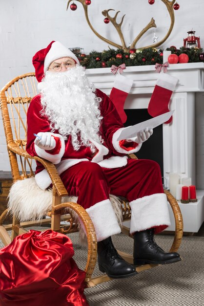 Père Noël assis dans une chaise berçante avec liste de souhaits