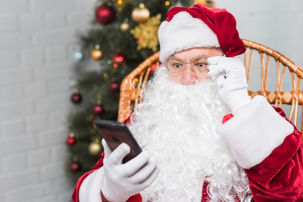 Père Noël assis sur un fauteuil à bascule et regardant un téléphone
