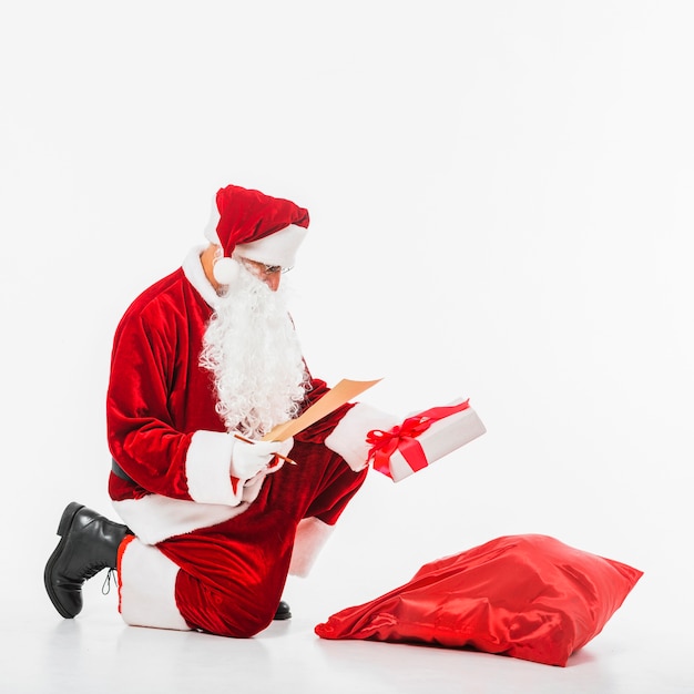 Père Noël assis avec sac de cadeaux et liste d&#39;enfants