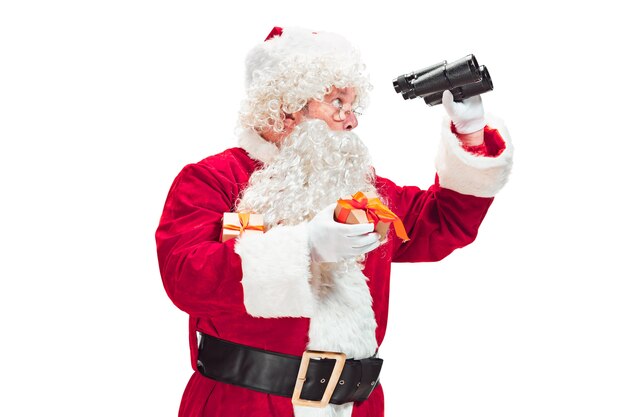 Père Noël avec une barbe blanche luxueuse, un chapeau du père Noël et un costume rouge isolé sur fond blanc avec des jumelles