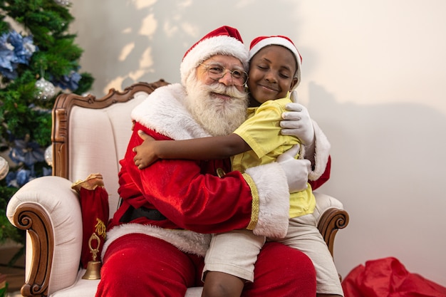 Le père noël distribue une boîte-cadeau à un petit garçon africain. étreinte