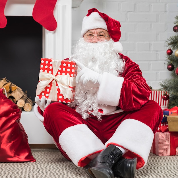 Père Noël à lunettes assis avec des coffrets cadeaux sur le sol