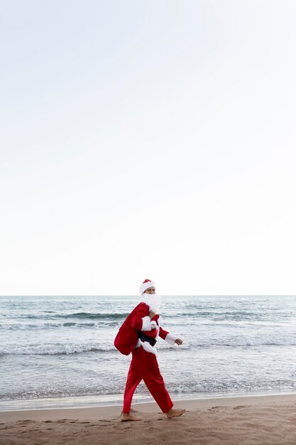 Père noël marchant sur la vue de côté de plage