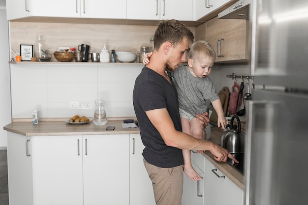 Père portant son fils montrant quelque chose sur le comptoir de la cuisine