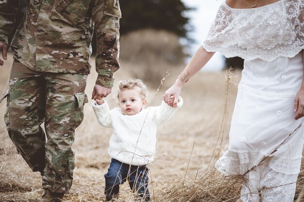 Père soldat avec sa femme tenant les mains de leur fils des deux côtés et marchant dans un champ