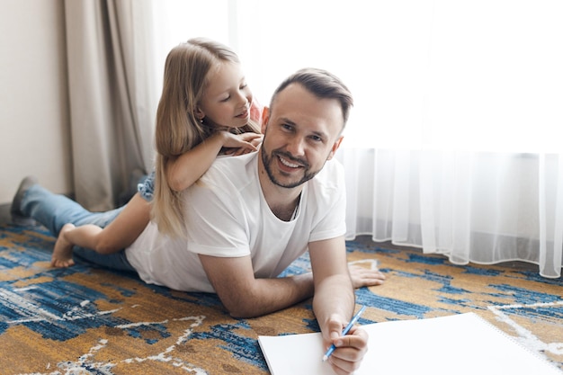 père souriant heureux et sa fille dessinant et faisant le travail à domicile à l'intérieur