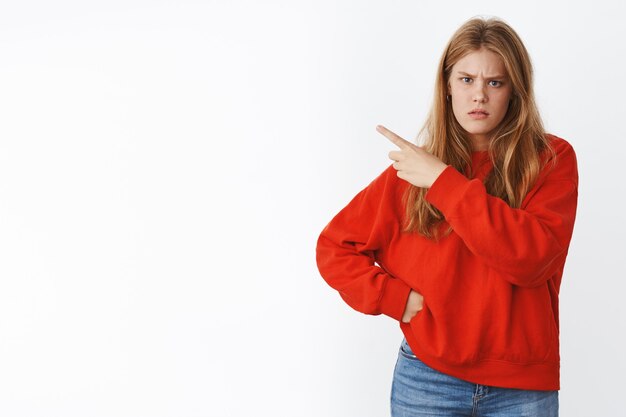 Perplexe et interrogée, intense, mécontente, sérieuse, jeune amie mignonne aux yeux bleus, aux taches de rousseur et aux cheveux blonds fronçant les sourcils mécontente, pointant vers la gauche, attendant des explications