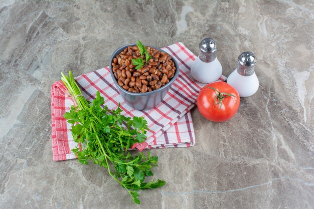 Persil, tomates, sel et bol de fèves au lard sur un tissu, sur le bleu.