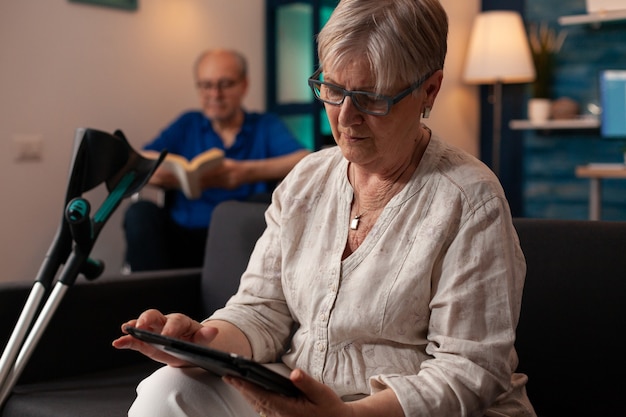 Personne âgée avec des béquilles regardant une tablette moderne