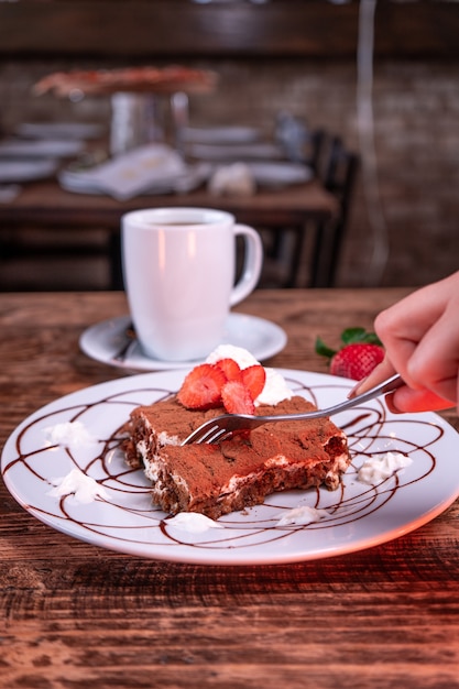 Photo gratuite personne coupant un biscuit au chocolat à la fraise à côté d'une tasse de café