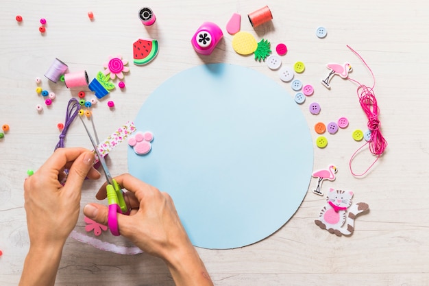 Une personne coupe le ruban avec des ciseaux sur le papier bleu avec des éléments décoratifs