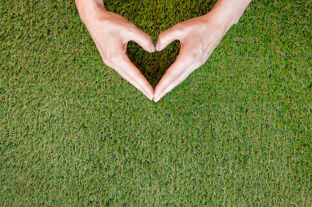 Photo gratuite personne faisant un coeur avec ses mains sur l'herbe avec espace copie