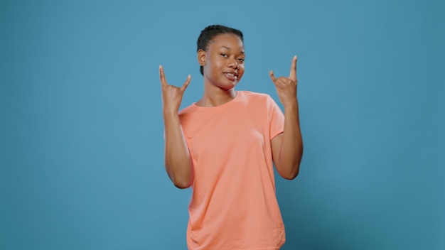 Personne ludique montrant un geste rock avec les mains à la caméra. Jeune femme faisant le symbole du rock and roll avec les doigts, se sentant excitée et ayant une expression faciale géniale. Adulte avec signe punk