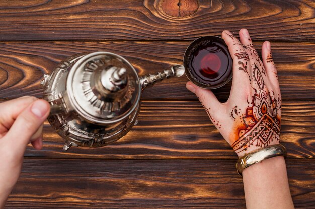 Personne avec mehndi verser le thé dans une petite tasse
