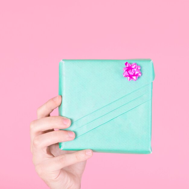 Une personne montrant une boîte cadeau turquoise enveloppée sur fond rose