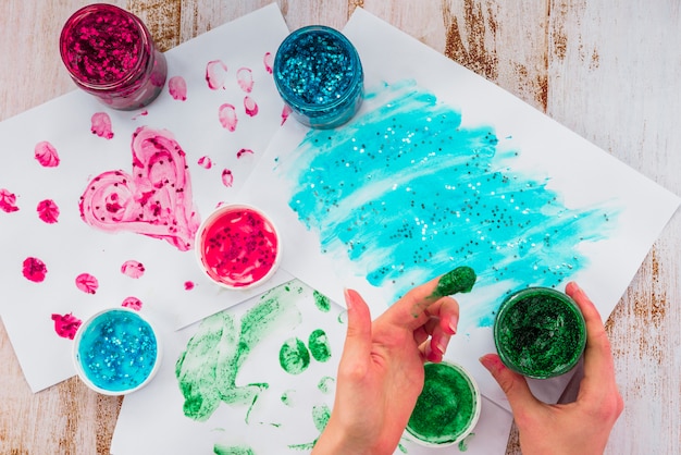 Photo gratuite personne peignant avec le doigt sur le papier en utilisant des couleurs de paillettes sur la table en bois