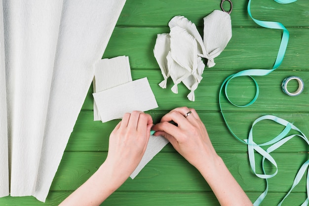 Personne qui fabrique de faux pétales à partir de papier crépon sur fond texturé vert