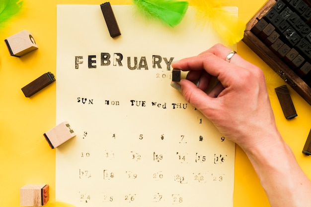 Photo gratuite une personne qui fait le calendrier de février avec des blocs typographiques sur fond jaune